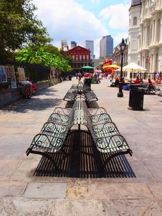 an iron bench sitting on the side of a road next to tall buildings and trees