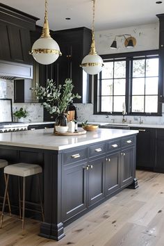 a large kitchen with black cabinets and white counter tops, gold pendant lights hanging from the ceiling