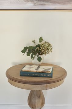 a wooden table topped with a book and a vase filled with flowers on top of it