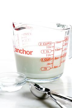 a measuring cup filled with milk next to spoons