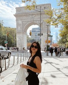 a woman is standing on the sidewalk in front of an arch