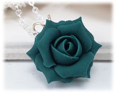 a green rose is sitting on a white surface next to a silver chain and necklace