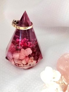 a pink vase filled with flowers next to a pair of gold earring clips on top of a white surface