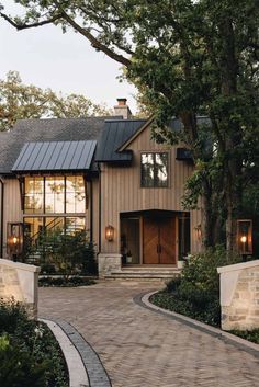 a house with a driveway and trees in the front yard, surrounded by greenery