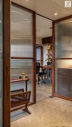 a wooden bench sitting in front of a glass wall with an office desk behind it