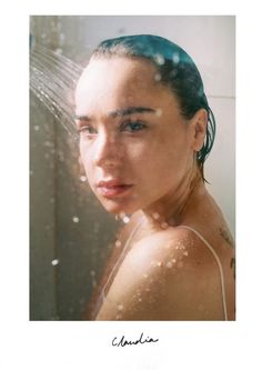 a woman with blue hair standing in front of a shower head and looking at the camera