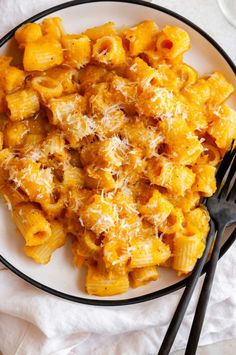 a white plate topped with macaroni and cheese next to two black utensils