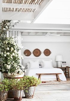 a bedroom with white bedding and plants in baskets