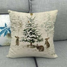 two pillows on a couch with christmas trees and bunnies in the snow behind them