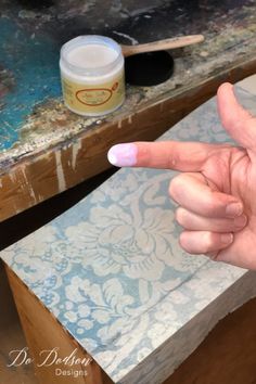 a person's hand pointing at something on a table next to a paintbrush