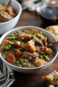 two bowls of beef stew with peas and bread on the side, one bowl is half eaten