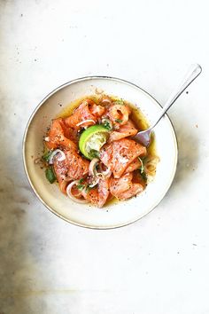 a white bowl filled with meat and vegetables on top of a marble counter next to a spoon