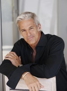 a man with grey hair and black shirt leaning on a wall