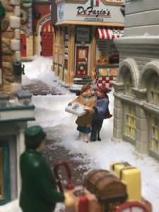 two people are walking down the street in front of some shops and buildings with snow on them