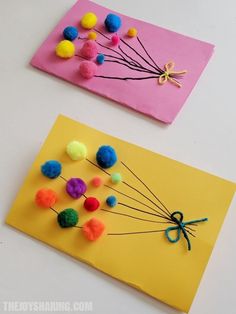 two paper cards with pom - poms and scissors on them, one is yellow and the other is pink