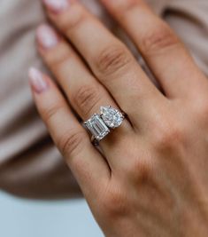 a woman's hand holding an engagement ring with three stones on it and the other side