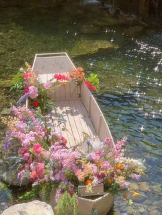 a row boat filled with flowers sitting on top of a river next to a body of water