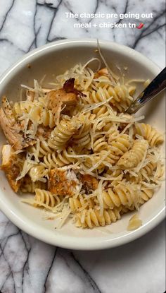 a white bowl filled with pasta and chicken on top of a marble countertop next to a fork