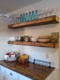 two wooden shelves above a kitchen counter with dishes and glasses on top of it,