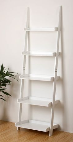 a white leaning shelf sitting on top of a wooden floor next to a potted plant