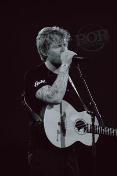 a man singing into a microphone while holding a guitar in front of his face and wearing a black t - shirt