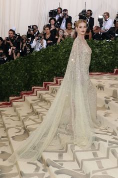 a woman in a white gown standing on top of a carpet with people taking pictures behind her