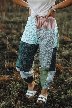 a woman standing in the grass with her hands on her hips wearing colorful pants and sandals