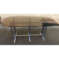 a glass table with two metal legs and a brown top is sitting on the ground