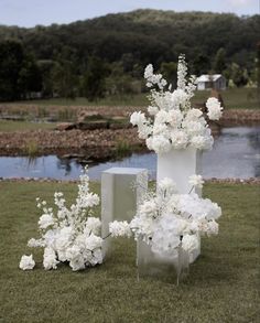 white flowers are arranged in tall vases on the grass next to a body of water