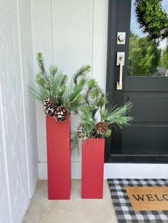 two tall red vases with pine cones and evergreen needles on the front door porch