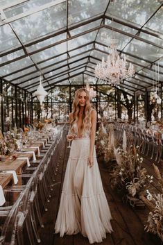 a woman in a white dress standing next to a long table with chairs and chandeliers