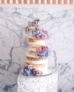 a three tiered cake with purple flowers on the top and happy birthday spelled in gold