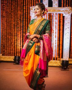 a woman in an orange and pink sari standing next to a stage with flowers on it