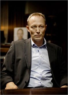 a man in a suit sitting at a desk with his hands on his hips and looking off to the side