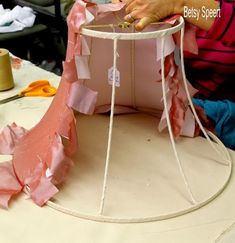 a woman is working on a pink and white cake with ribbon trimming around it