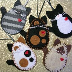 four felt cat ornaments are hanging on a string with red buttons and black, white, gray, and brown cats