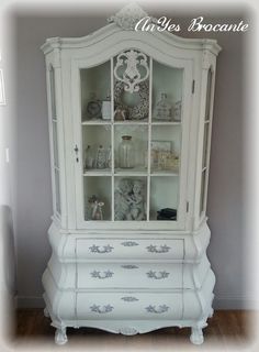 a white china cabinet with glass doors and shelves in the middle, painted to look like an old fashioned hutch