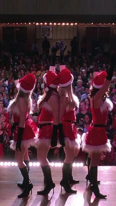 three women dressed in santa claus outfits dancing on stage with people watching from the audience