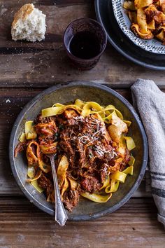 a plate of pasta with meat and sauce on it next to a glass of wine