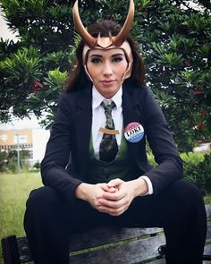 a woman sitting on top of a wooden bench wearing a suit and horned headdress