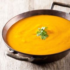 a wooden bowl filled with carrot soup and garnished with parsley on top