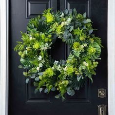 a wreath is hanging on the front door with green leaves and white flowers around it