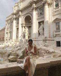 a woman in a white dress is sitting on a ledge looking at her cell phone