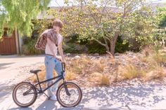 a young man is standing next to his bike in front of some bushes and trees