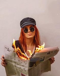 a woman with red hair wearing sunglasses and a hat is holding a newspaper in front of her face