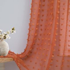 a vase filled with white flowers sitting on top of a table next to a curtain