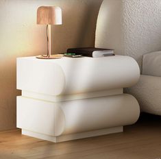 a white nightstand with a lamp on top of it next to a bed in a room