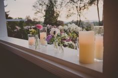 candles and flowers sit on a window sill