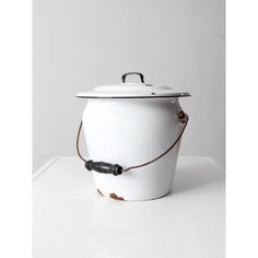 a white pot with a brown cord around the handle and lid on a white table