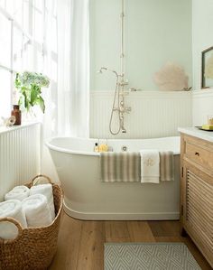 a white bath tub sitting in a bathroom next to a wooden dresser and window with curtains